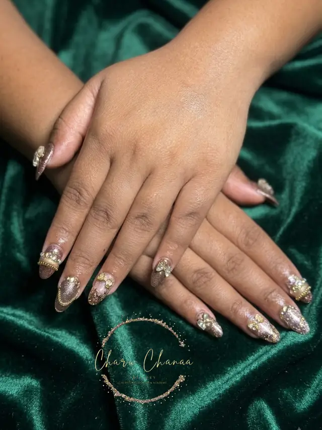 A hand resting on green velvet with long glitter-finished nail extensions, the salon's own script logo below.